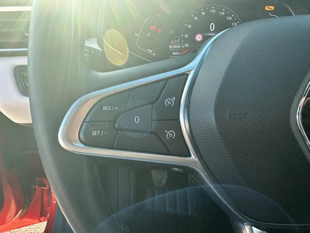 Gros plan sur le volant cuir de la Renault Clio rouge foncé, montrant les commandes du régulateur de vitesse côté gauche.