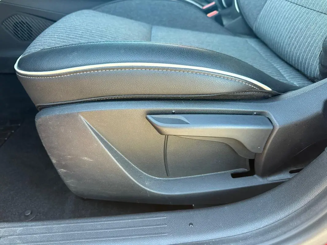 Gros plan sur l'accoudoir central en cuir noir avec surpiqûres blanches, siège tissu gris de la Renault Clio rouge foncé.