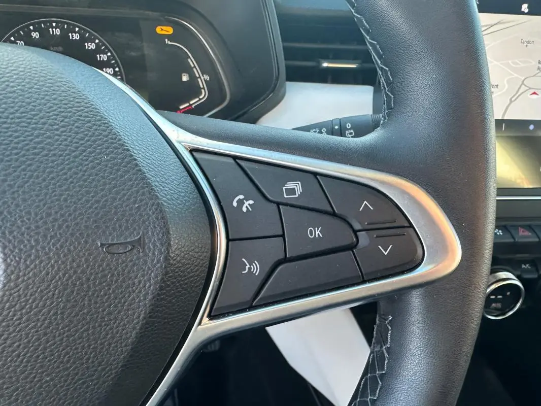 Gros plan sur le volant cuir de la Renault Clio rouge foncé 2021, avec commandes multifonctions et tableau de bord partiellement visible.