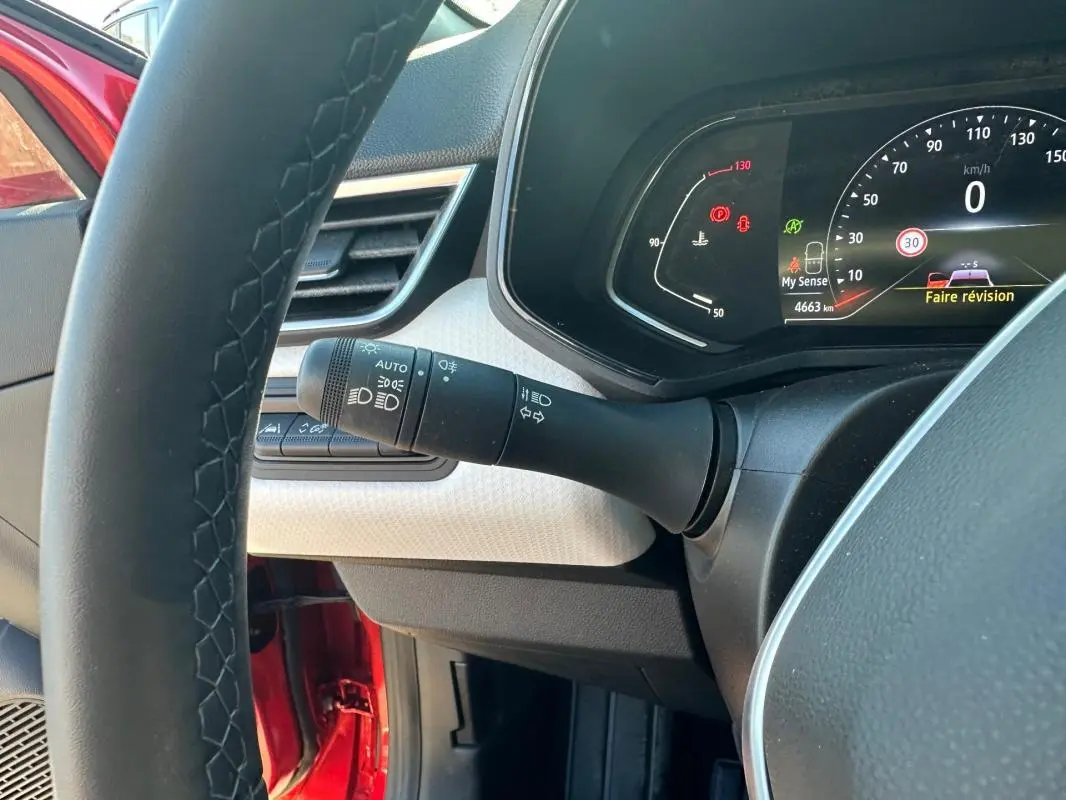 Vue intérieure côté conducteur de la Renault Clio rouge foncé 2021, tableau de bord et volant cuir visibles.