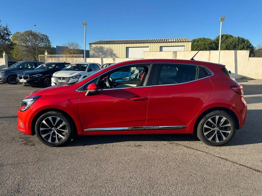 Profil côté gauche d'une Renault Clio rouge foncé de 2021 avec jantes alliage 17 pouces sur un parking extérieur.
