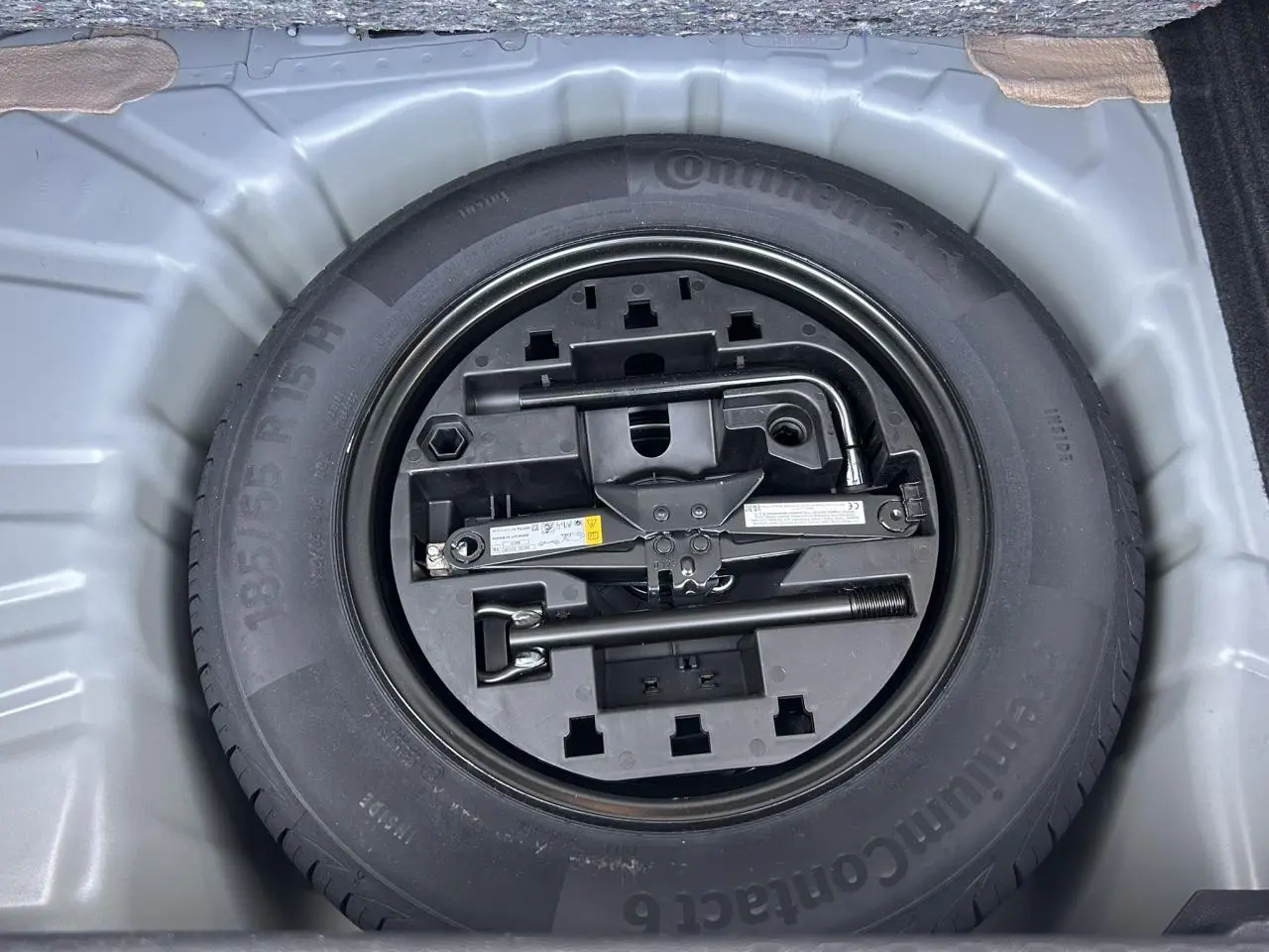 Vue plongeante sur la roue de secours tôle et ses outils dans le coffre de la Renault Clio Gris Rafale 2025.