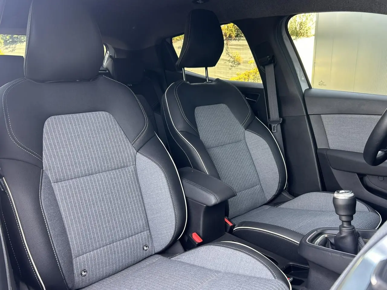 Vue intérieure rapprochée des sièges avant gris et noirs avec accoudoir central et levier de vitesse manuel d’une Renault Clio 2025.