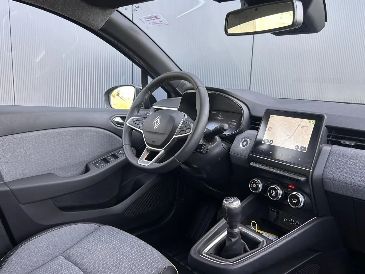 Vue intérieure côté conducteur de la Renault Clio 2025, volant multifonction, écran tactile et levier de vitesses manuel.