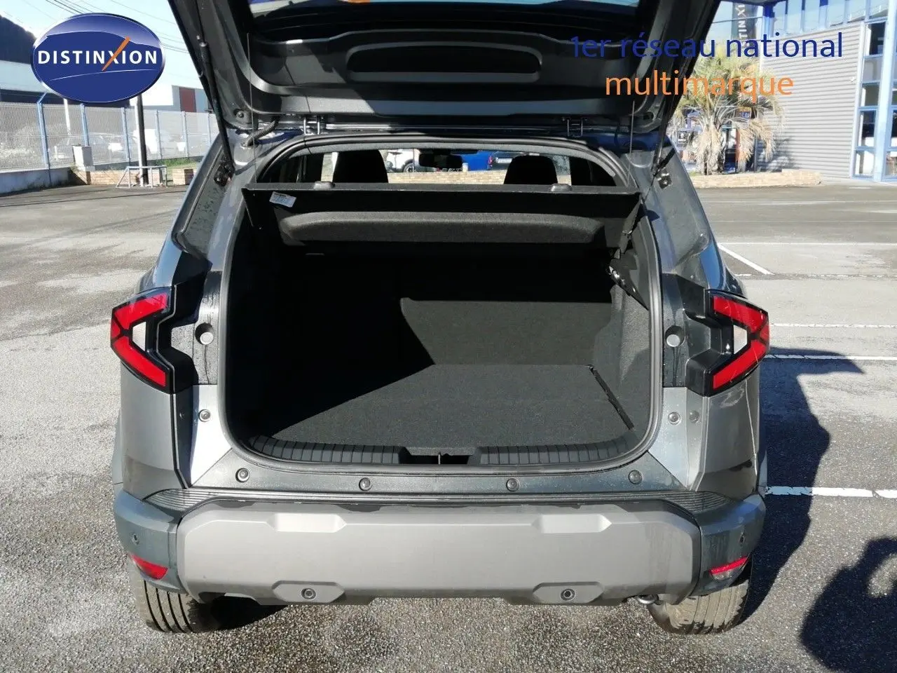 Vue arrière du Dacia Duster gris schiste métal 2026 avec coffre ouvert sur parking extérieur.