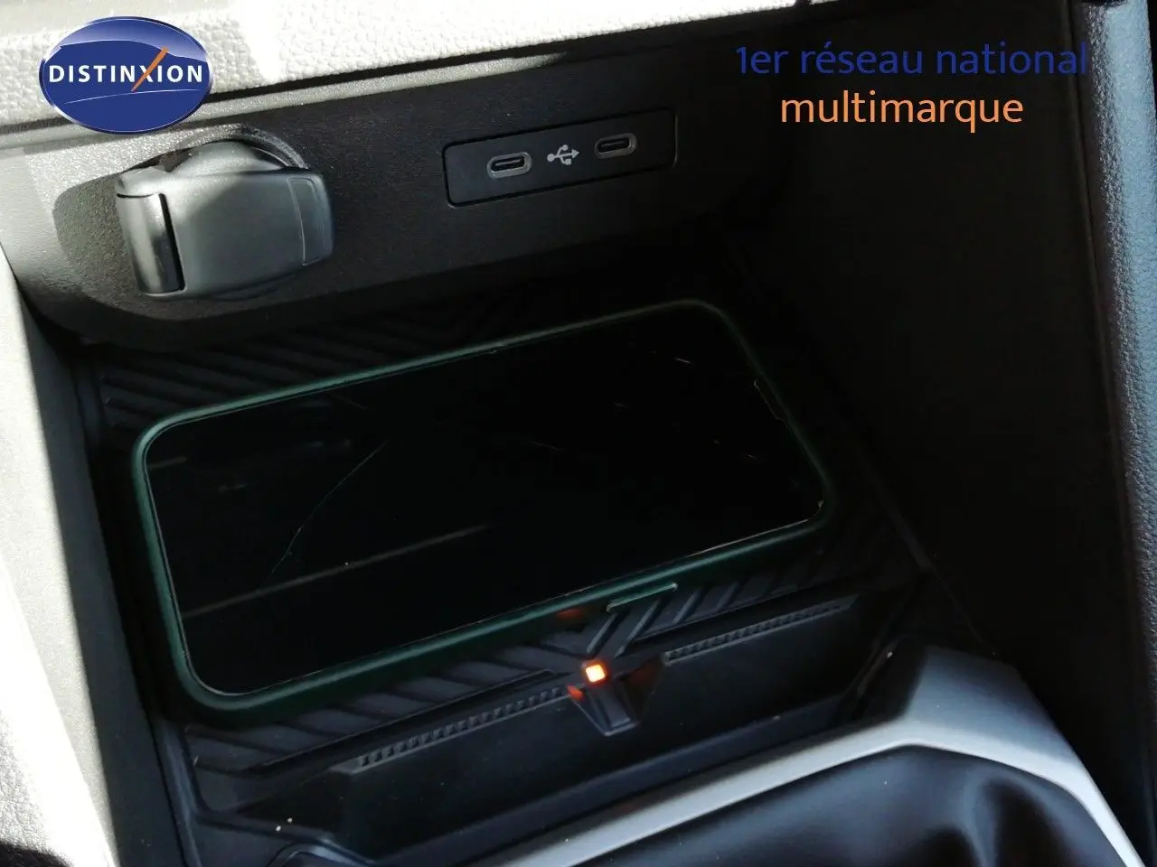 Détail de la console centrale du Dacia Duster 2026, zone de recharge sans fil avec smartphone posé, intérieur gris noir.