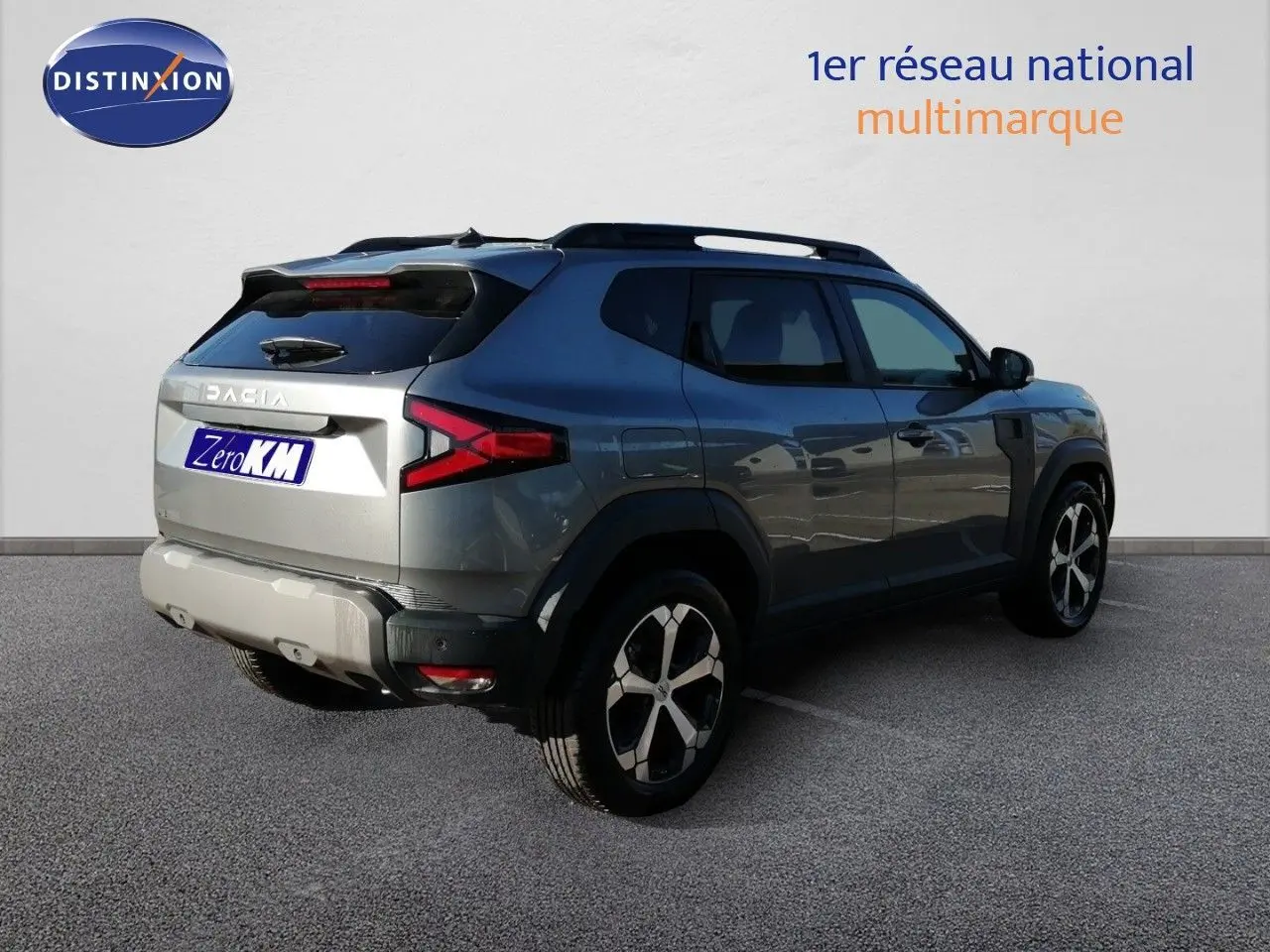 Vue 3/4 arrière droit du Dacia Duster gris schiste métal avec jantes bicolores et barres de toit visibles.