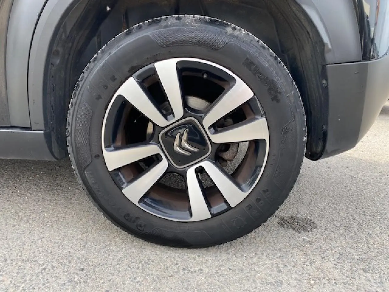 Gros plan sur la roue galette noire et argentée du côté gauche d’un Citroën C3 Aircross noir de 2019.