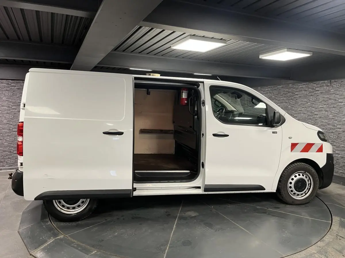 Vue de profil côté droit d'un utilitaire Citroën Jumpy blanc avec porte coulissante ouverte et marquages rouges sur l'aile avant.