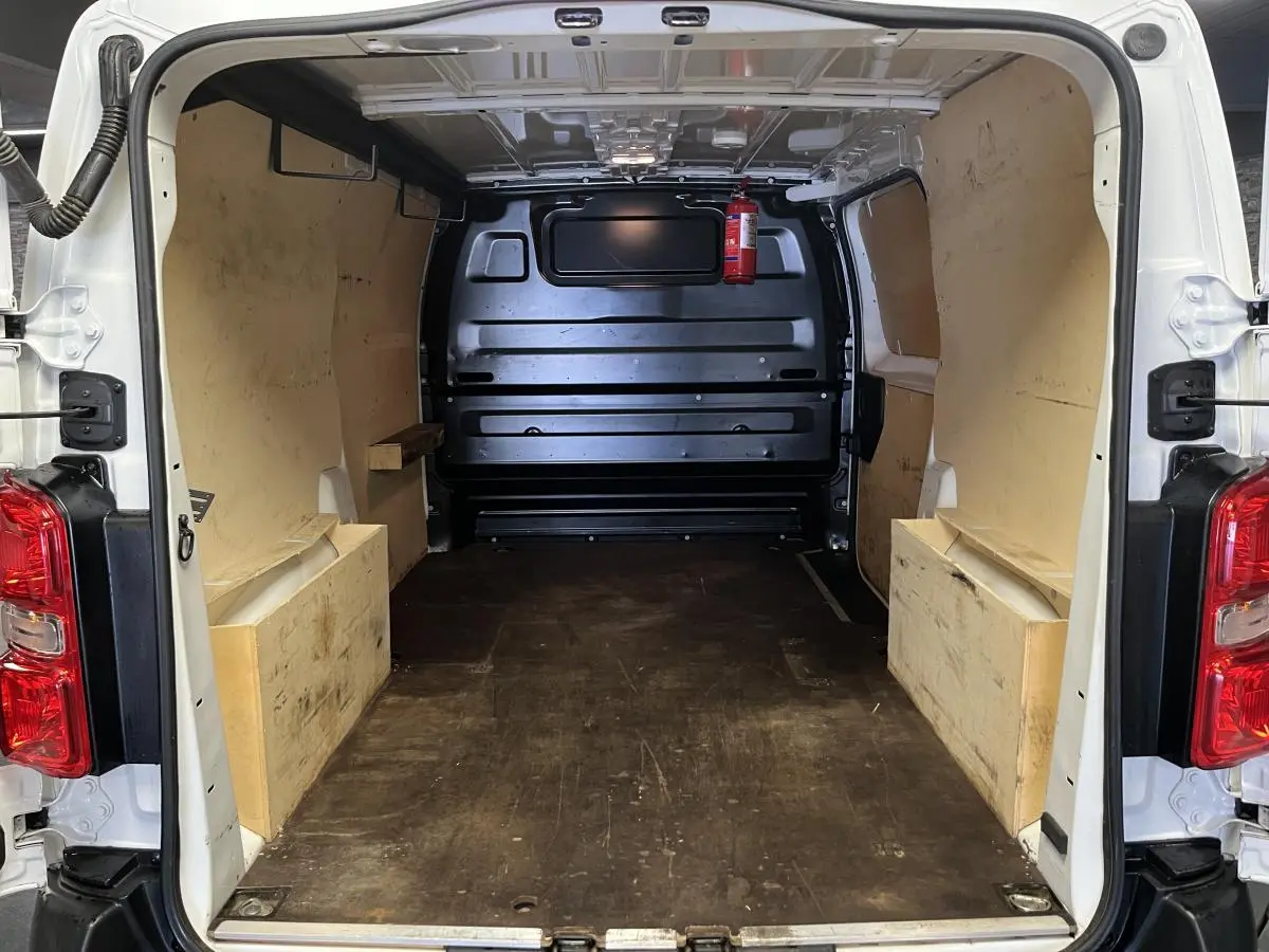 Intérieur du coffre arrière ouvert d'un Citroën Jumpy blanc, montrant le plancher et habillage bois latéral.