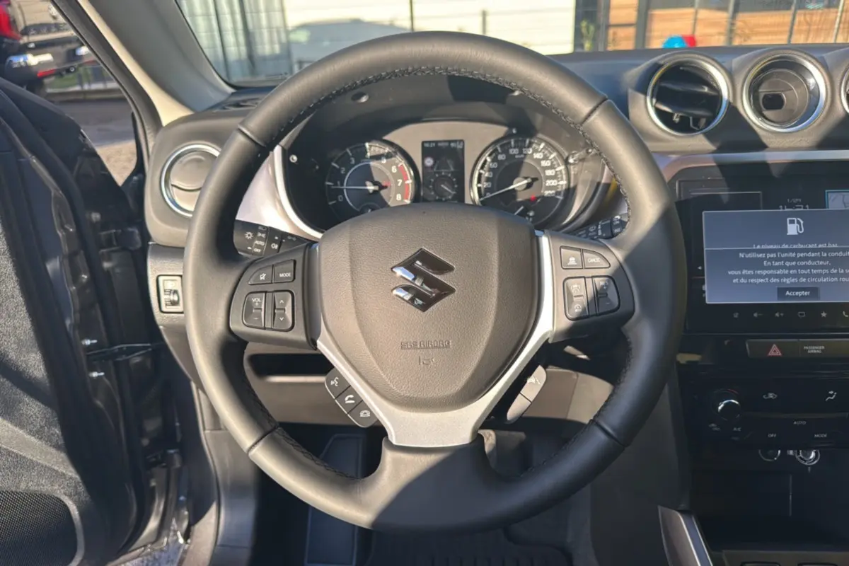 Vue intérieure centrée sur le volant noir du Suzuki Vitara 2025, avec tableau de bord et écran tactile allumé.