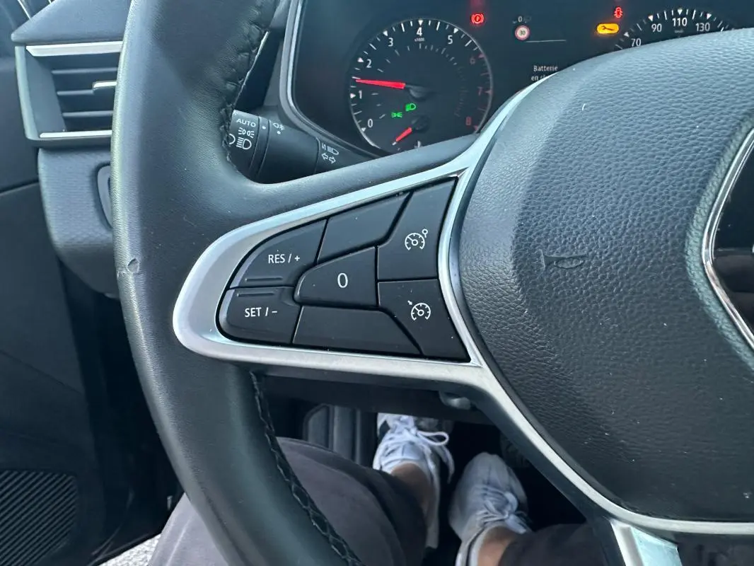 Gros plan sur le volant noir de la Renault Clio 2022, montrant les commandes du régulateur de vitesse côté gauche.