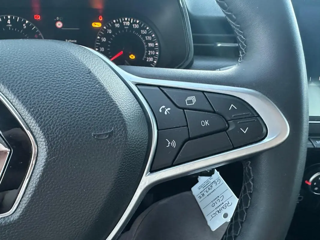 Gros plan sur le volant noir de la Renault Clio gris foncé 2022, avec commandes multifonctions et tableau de bord éclairé.