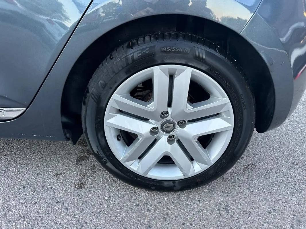 Gros plan sur la roue arrière droite d'une Renault Clio gris foncé, mettant en valeur la jante alliage au design moderne.
