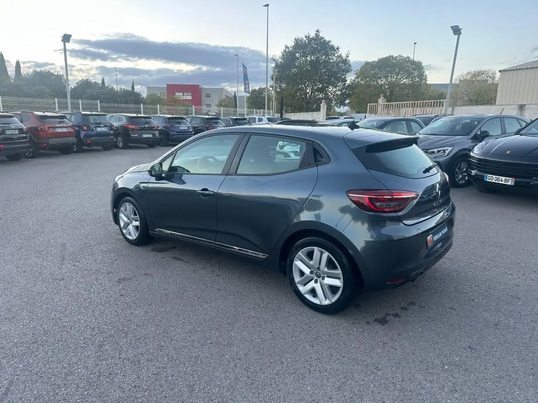 Renault Clio gris foncé vue 3/4 arrière droit sur parking, avec jantes alliage et vitres teintées.