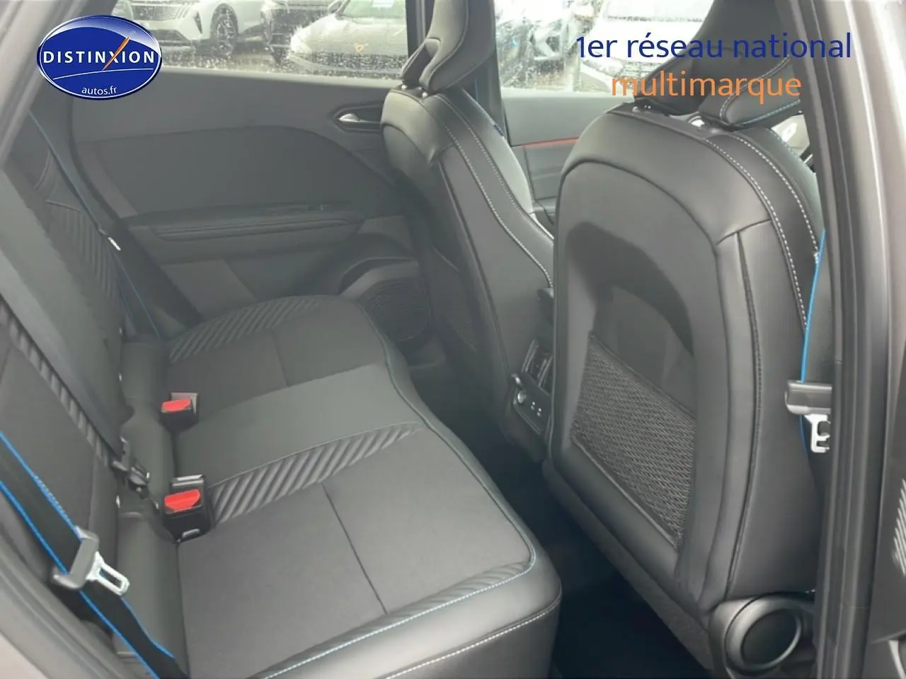 Vue intérieure arrière côté gauche du Renault Captur gris cassiopée, sièges noirs avec surpiqûres bleues et rangements filet au dos des sièges avant.