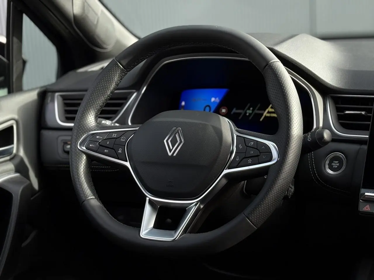 Vue rapprochée du volant noir perforé de la Renault SYMBIOZ 2025 avec commandes intégrées et tableau de bord numérique bleu.