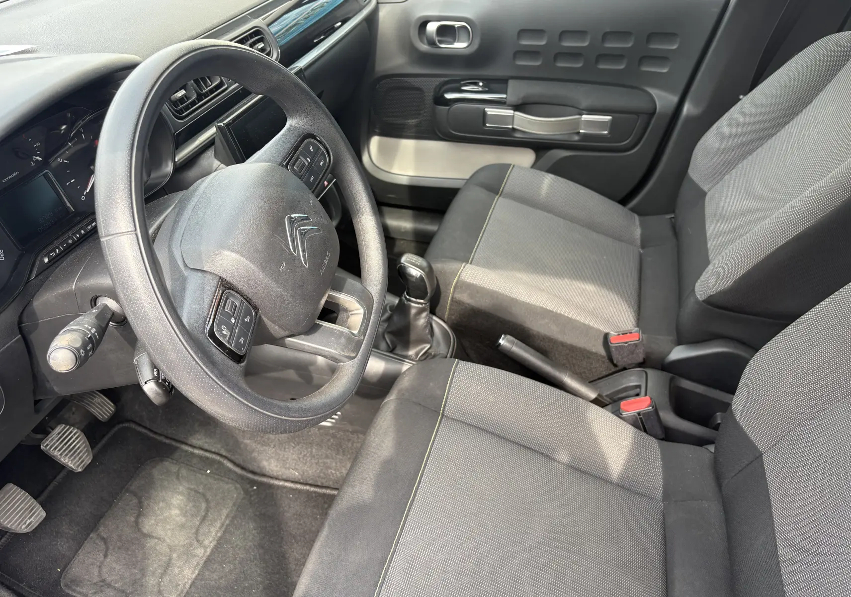 Vue intérieure côté conducteur de la Citroën C3 blanche 2019, volant multifonction et sièges tissu gris.