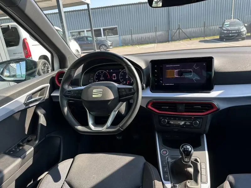 Vue intérieure de face du poste de conduite du SEAT Arona 2025 avec volant multifonction, écran tactile et détails rouges autour des aérateurs.