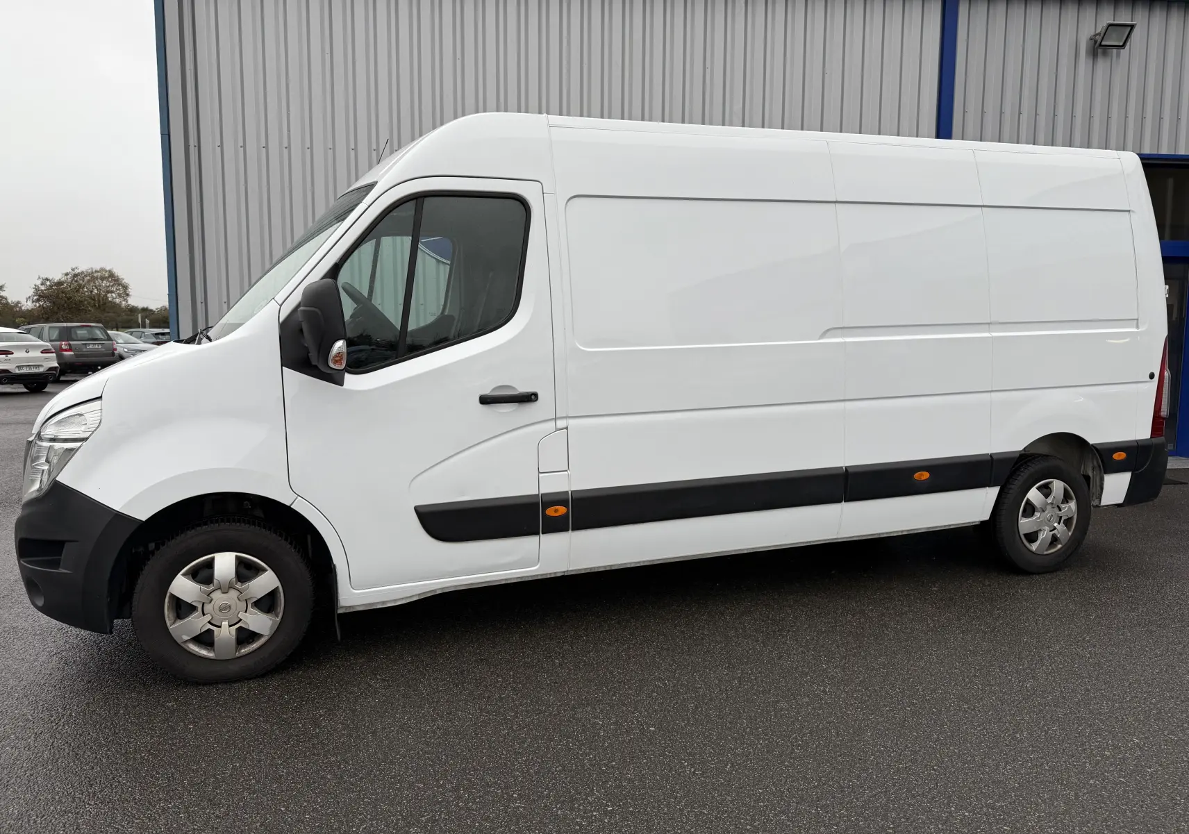 Fourgon Nissan NV400 blanc vu de profil côté gauche, avec protections noires et jantes acier.