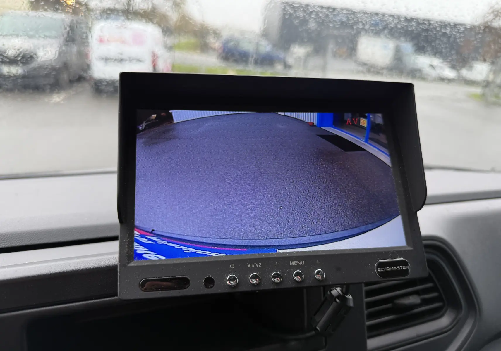 Écran de caméra de recul dans un Nissan NV400 blanc, vue intérieure du tableau de bord avec pluie sur le pare-brise.