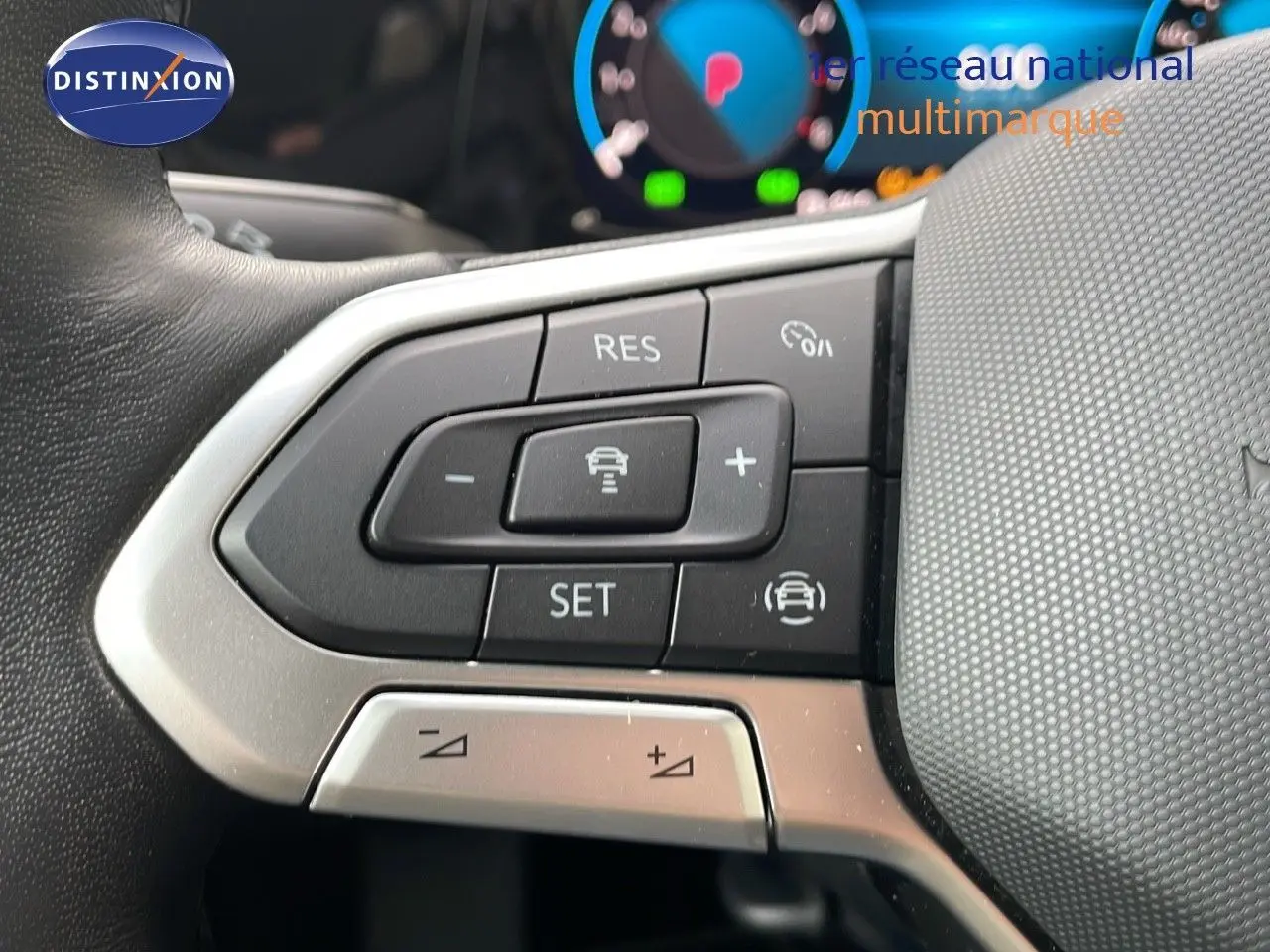 Gros plan sur les commandes au volant côté gauche d'une Volkswagen Golf VIII bleu lapiz metal, avec tableau de bord numérique flou.