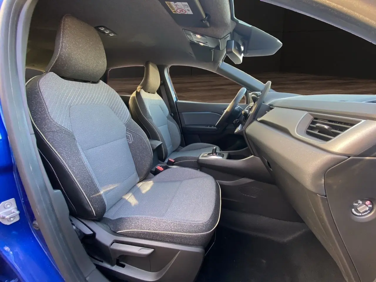 Vue intérieure côté gauche du Renault Captur 2025 bleu Iron avec sièges tissu gris et tableau de bord épuré.
