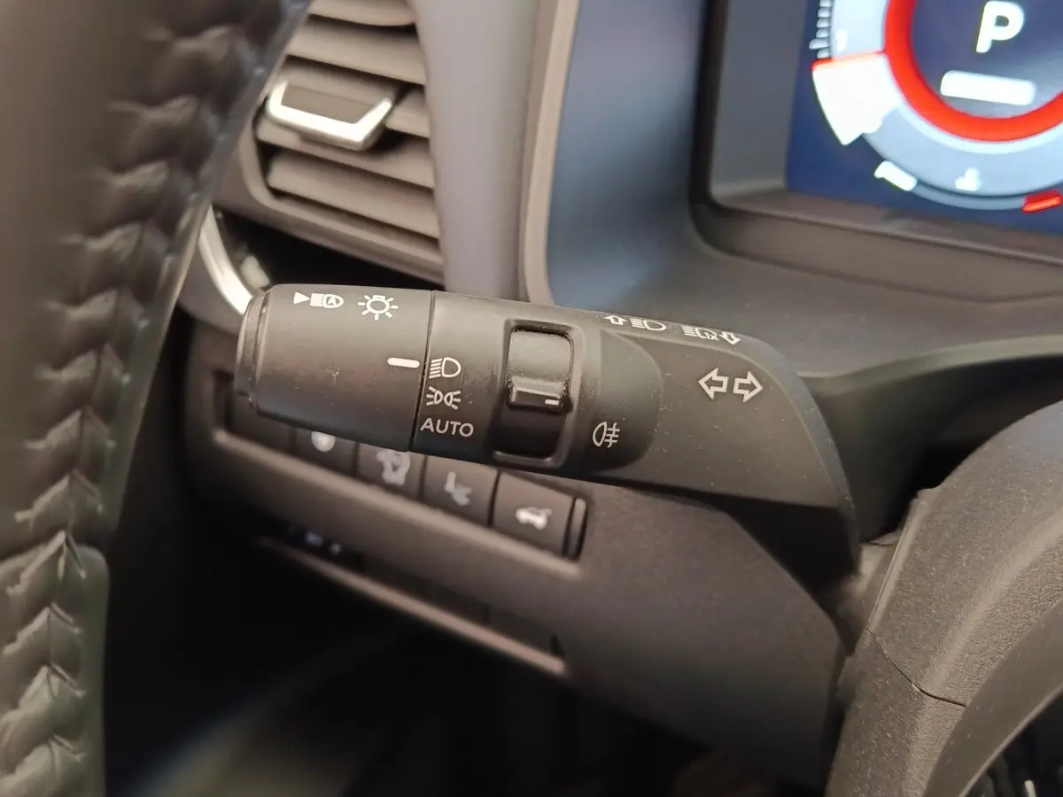 Gros plan sur la commande des phares et clignotants du Nissan Qashqai noir, avec tableau de bord numérique en arrière-plan.