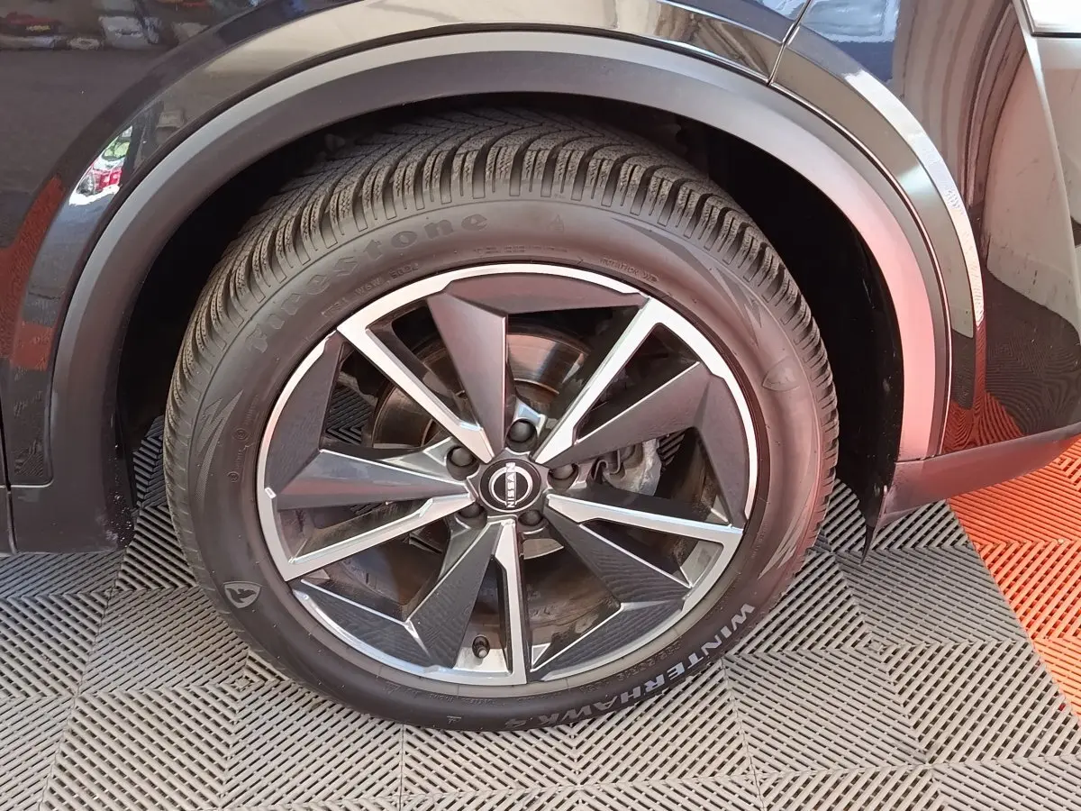 Gros plan sur la roue avant droite noire du Nissan Qashqai 2023 avec jante alliage et pneu Firestone.