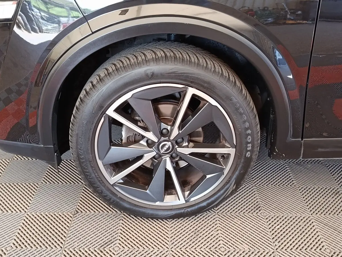 Gros plan sur la roue avant gauche noire du Nissan Qashqai 2023 avec jante alliage bicolore et pneu Firestone.