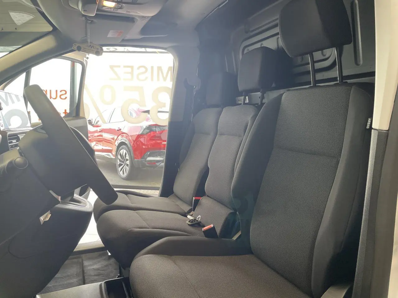 Vue intérieure côté conducteur du Peugeot Partner blanc, montrant la banquette passager 2 places en tissu noir avec appuis-tête.