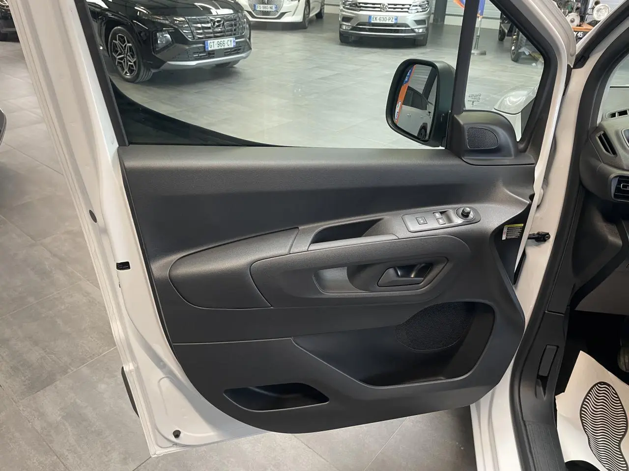 Vue rapprochée de la porte avant gauche blanche du Peugeot Partner 2026 avec commandes électriques et poignée noire.