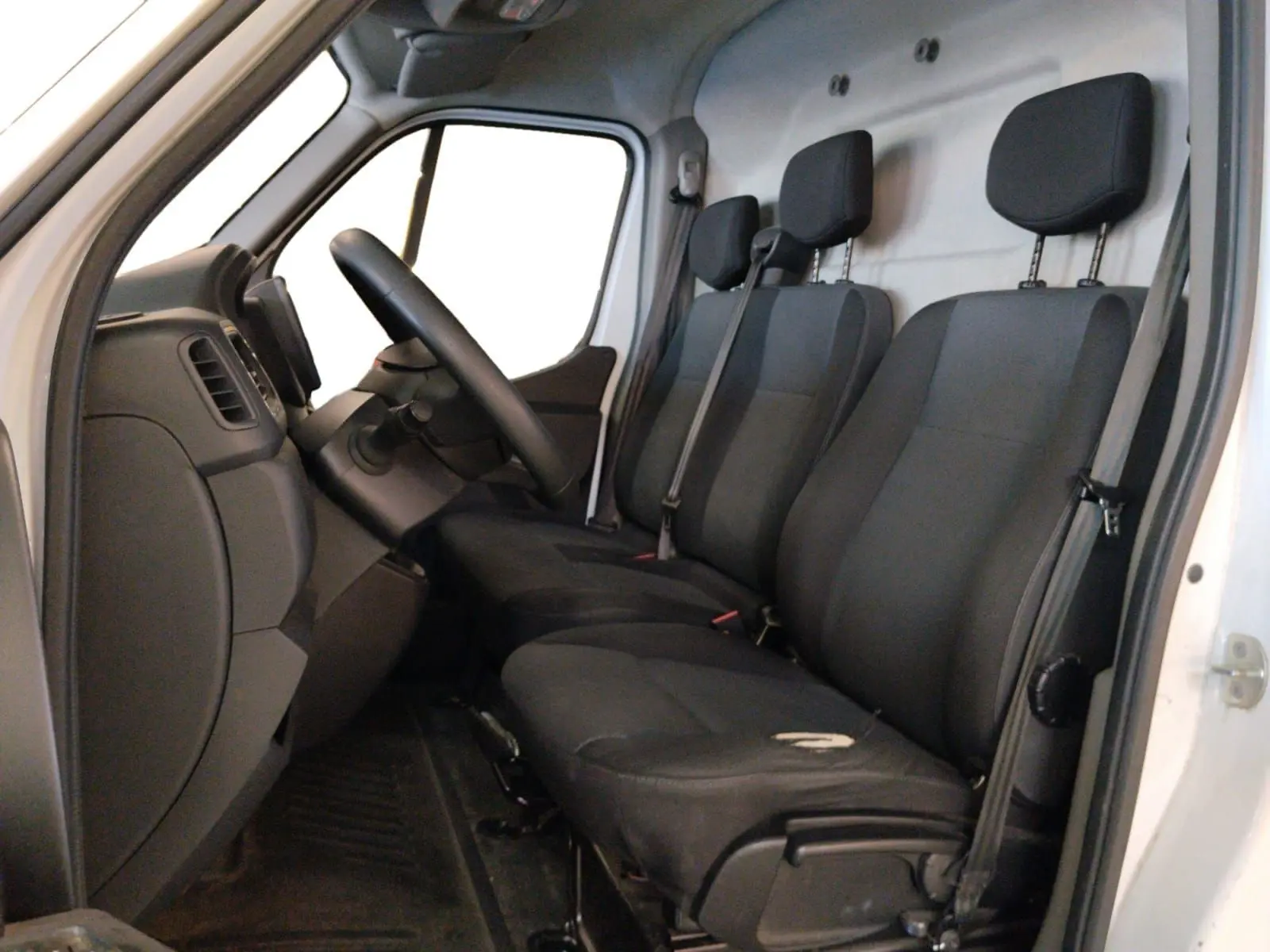 Vue intérieure côté conducteur du Renault Master blanc 2023, montrant les trois sièges noirs et le tableau de bord simple.
