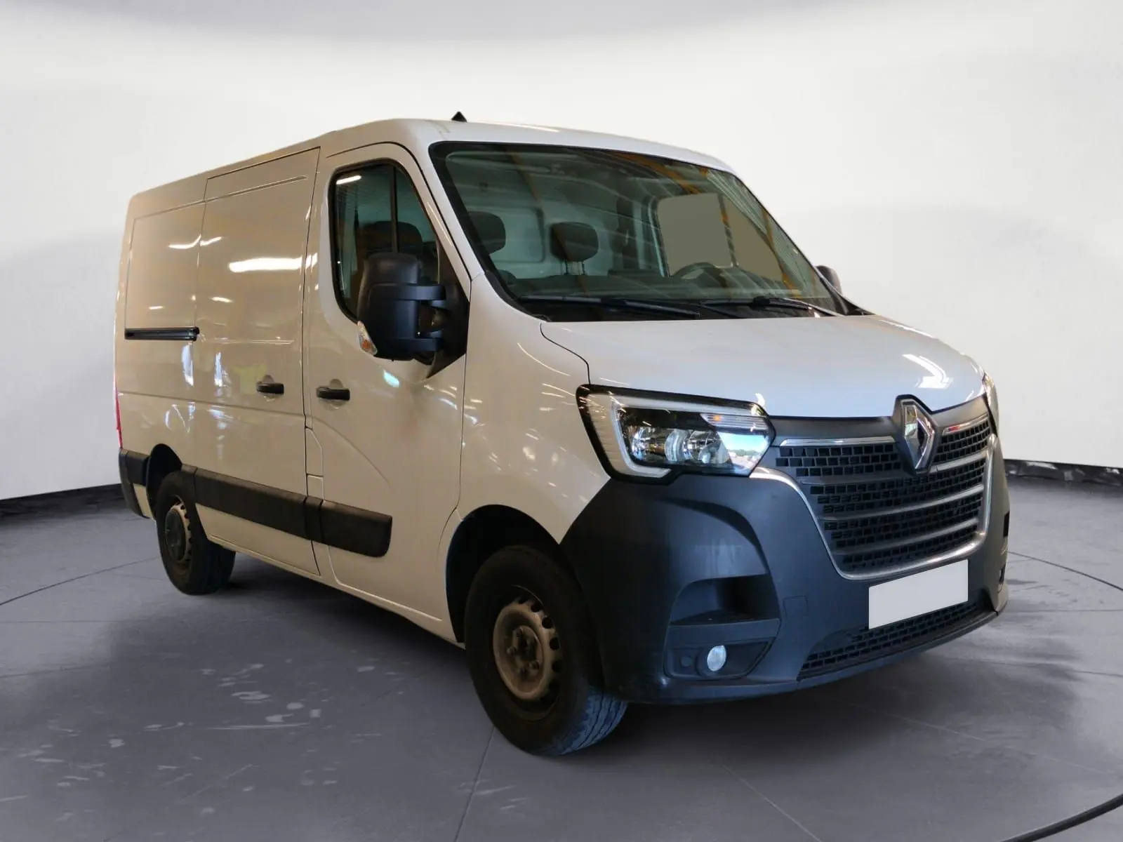 Vue 3/4 avant d’un Renault Master blanc avec pare-chocs noirs et cabine utilitaire, sur fond neutre intérieur.