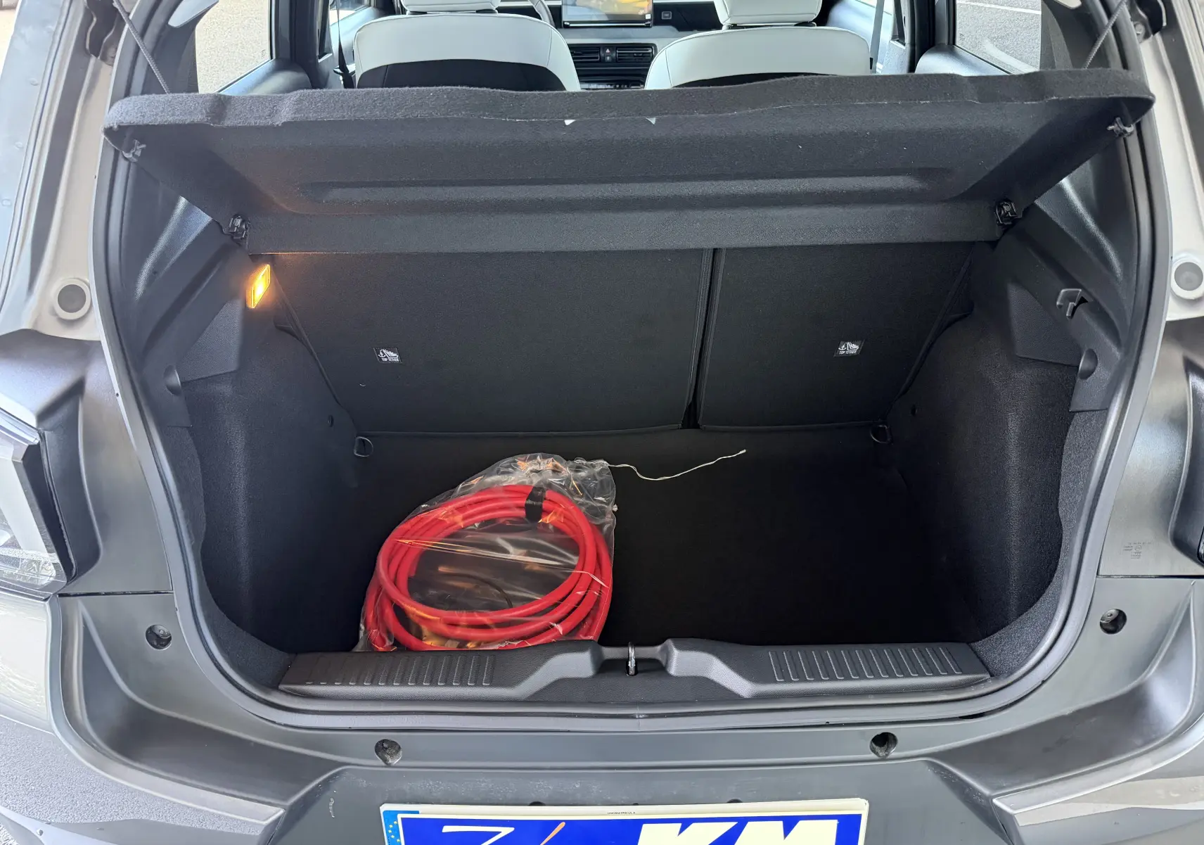 Coffre ouvert d'une Citroën E-C3 113 MAX gris Mercury, avec câble de recharge électrique rouge visible à l'intérieur.