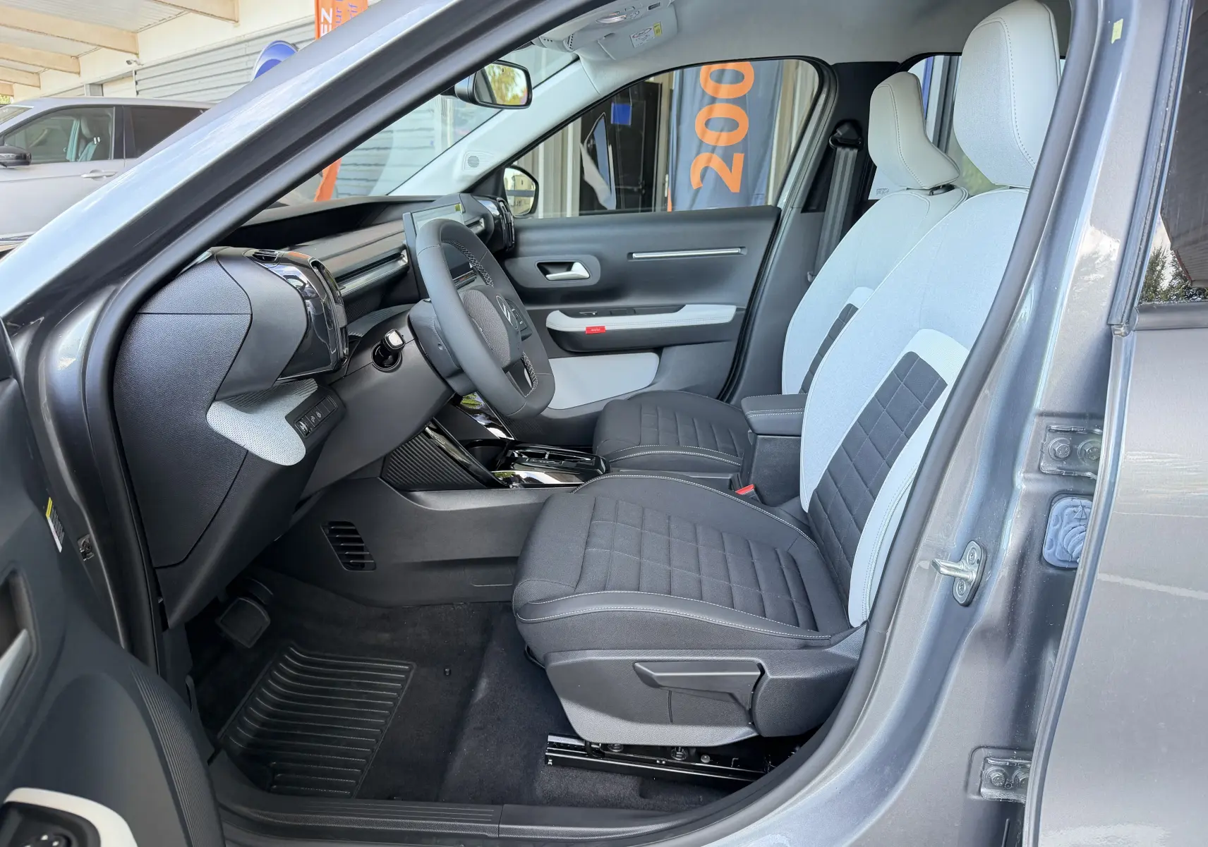 Vue intérieure côté conducteur de la Citroën E-C3 113 MAX gris Mercury, avec sellerie tissu noir et clair bicolore.