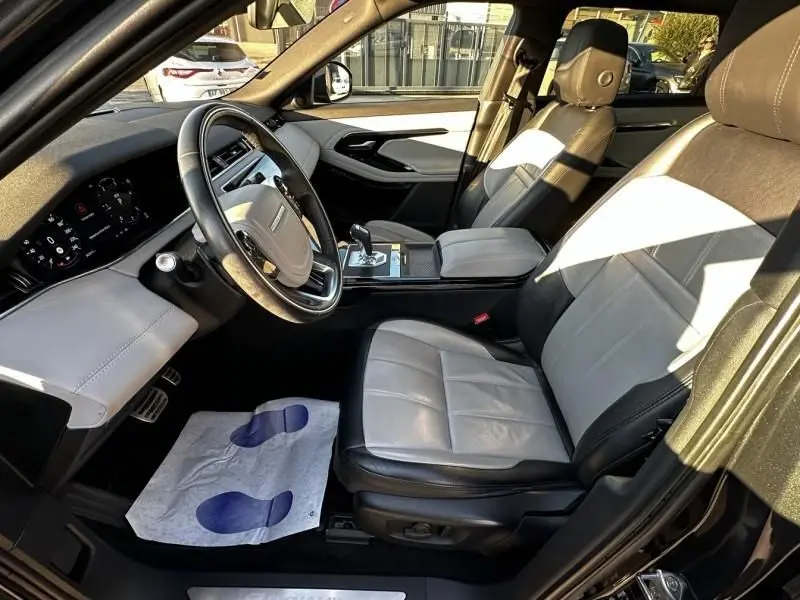 Intérieur du Range Rover Evoque 2019 vu côté conducteur, sièges cuir bicolores gris clair et noir, tableau de bord moderne.