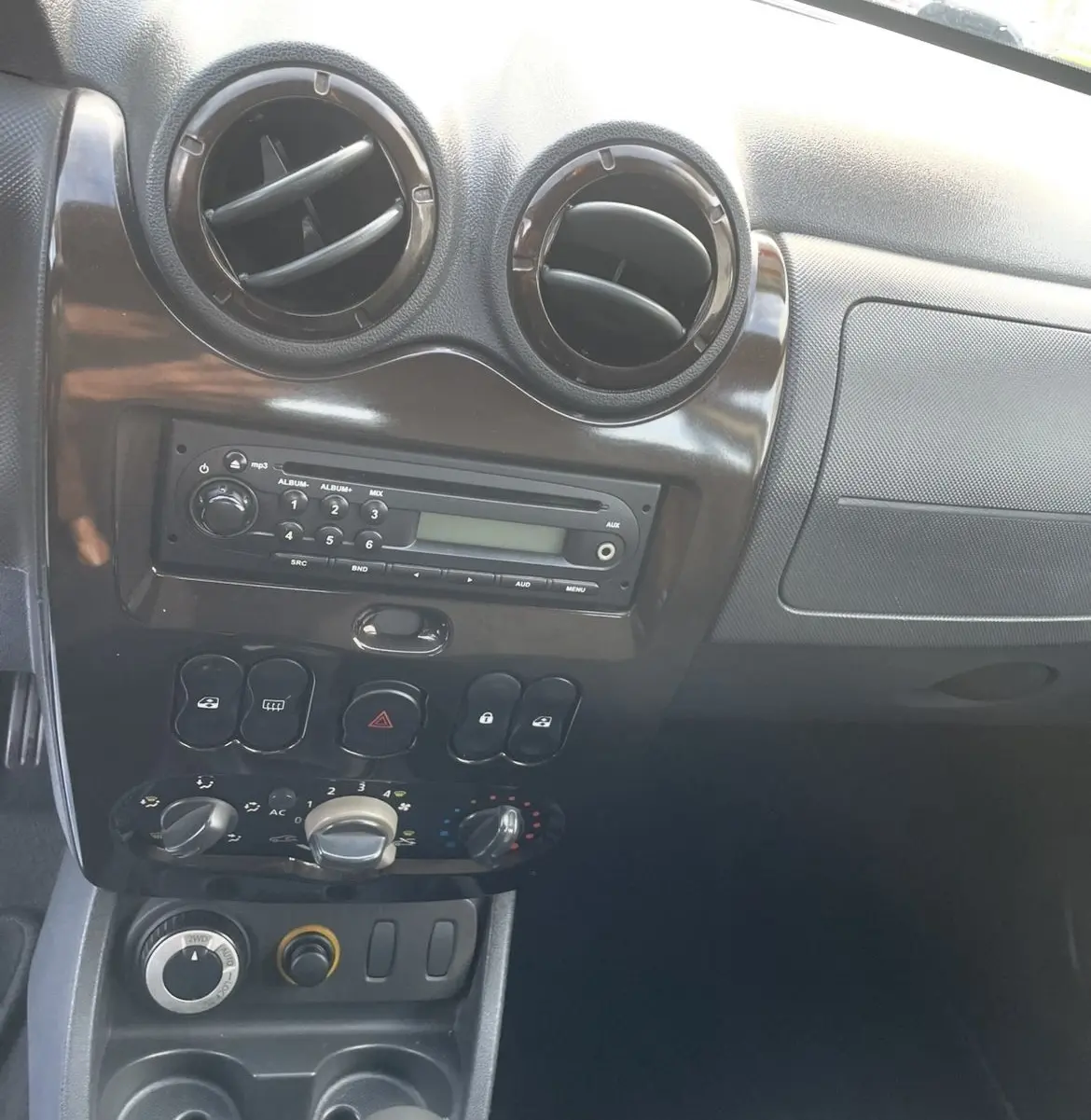 Vue rapprochée du tableau de bord gris foncé du Dacia Duster 2011, avec commandes climatisation et levier de vitesses manuel.