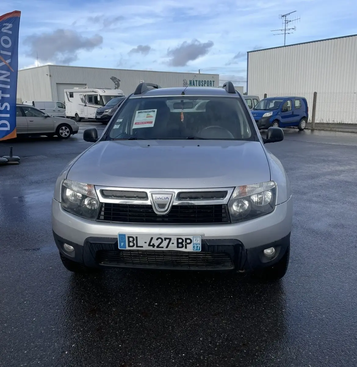 Vue frontale d'un Dacia Duster gris 2011 avec barres de toit et plaque d'immatriculation française visible.