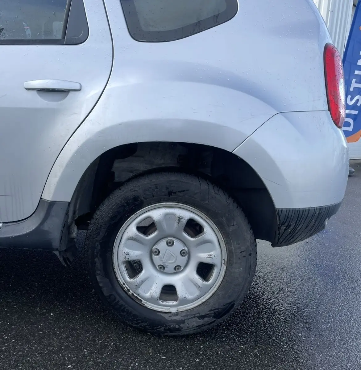 Dacia Duster gris vue du côté arrière droit, mettant en valeur la roue arrière avec enjoliveur et la vitre teintée.
