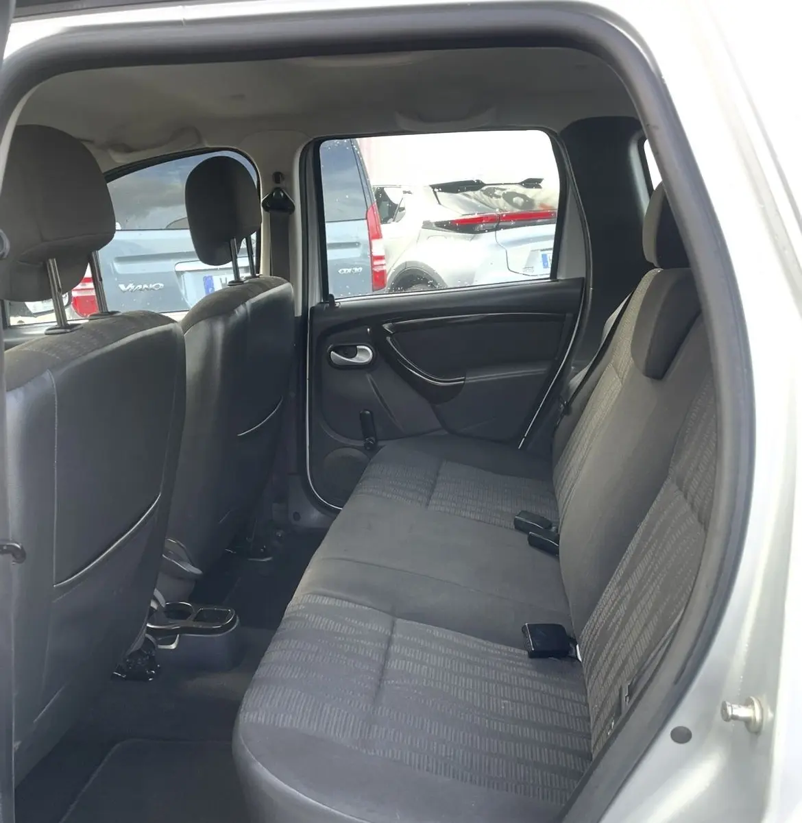 Vue intérieure arrière droite du Dacia Duster gris montrant la banquette 1/3-2/3 et les sièges en tissu noir.