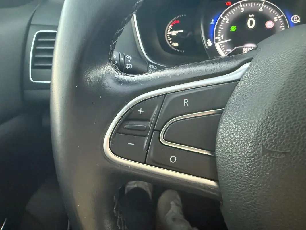 Gros plan sur le volant cuir de la Renault Mégane IV gris clair, avec commandes intégrées et tableau de bord en arrière-plan.