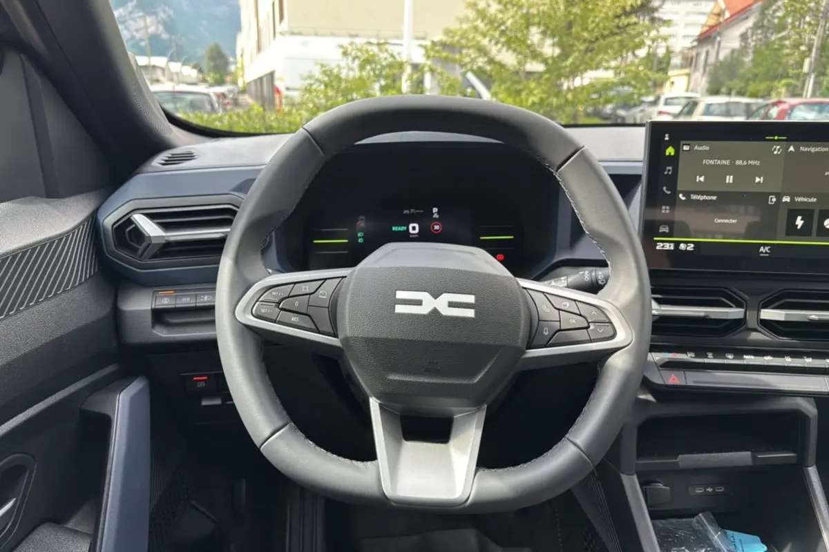 Vue intérieure centrée sur le volant cuir du Dacia Duster 2026, avec tableau de bord numérique et écran tactile central.