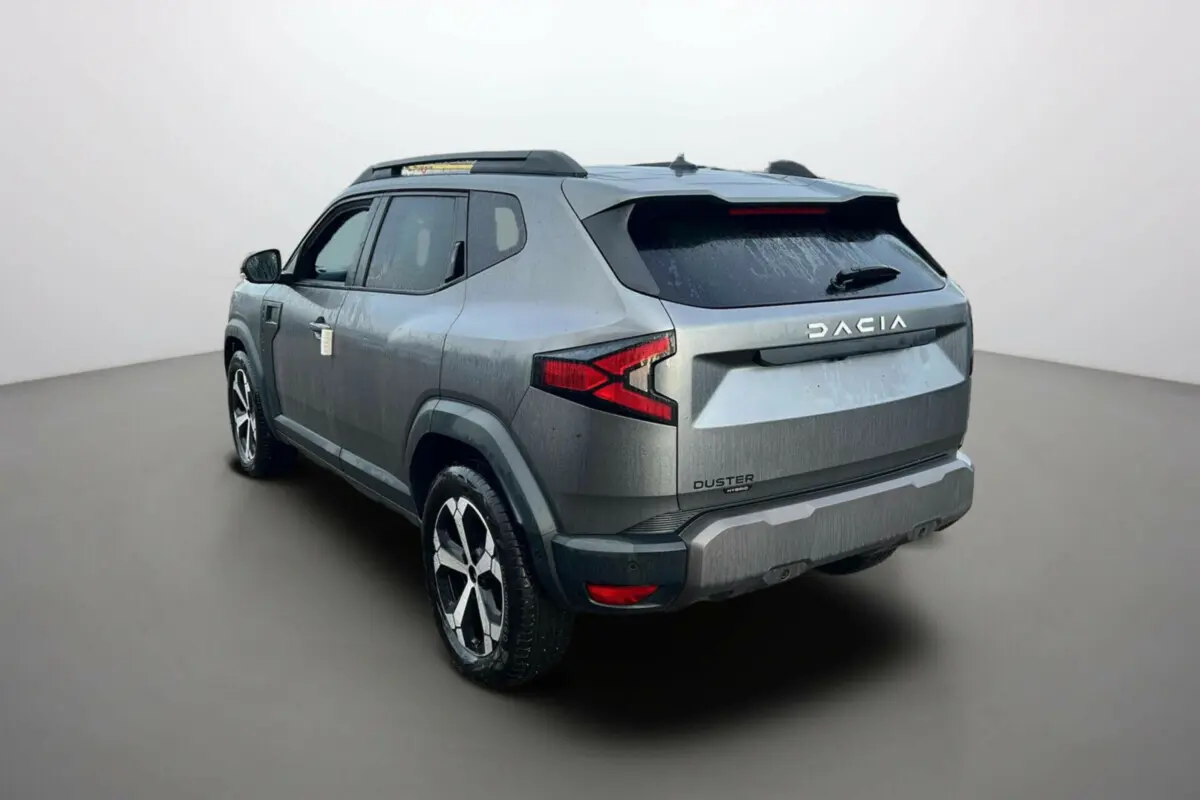 Vue 3/4 arrière droite d'un Dacia Duster noir nacré avec jantes alu 18 pouces et barres de toit visibles.
