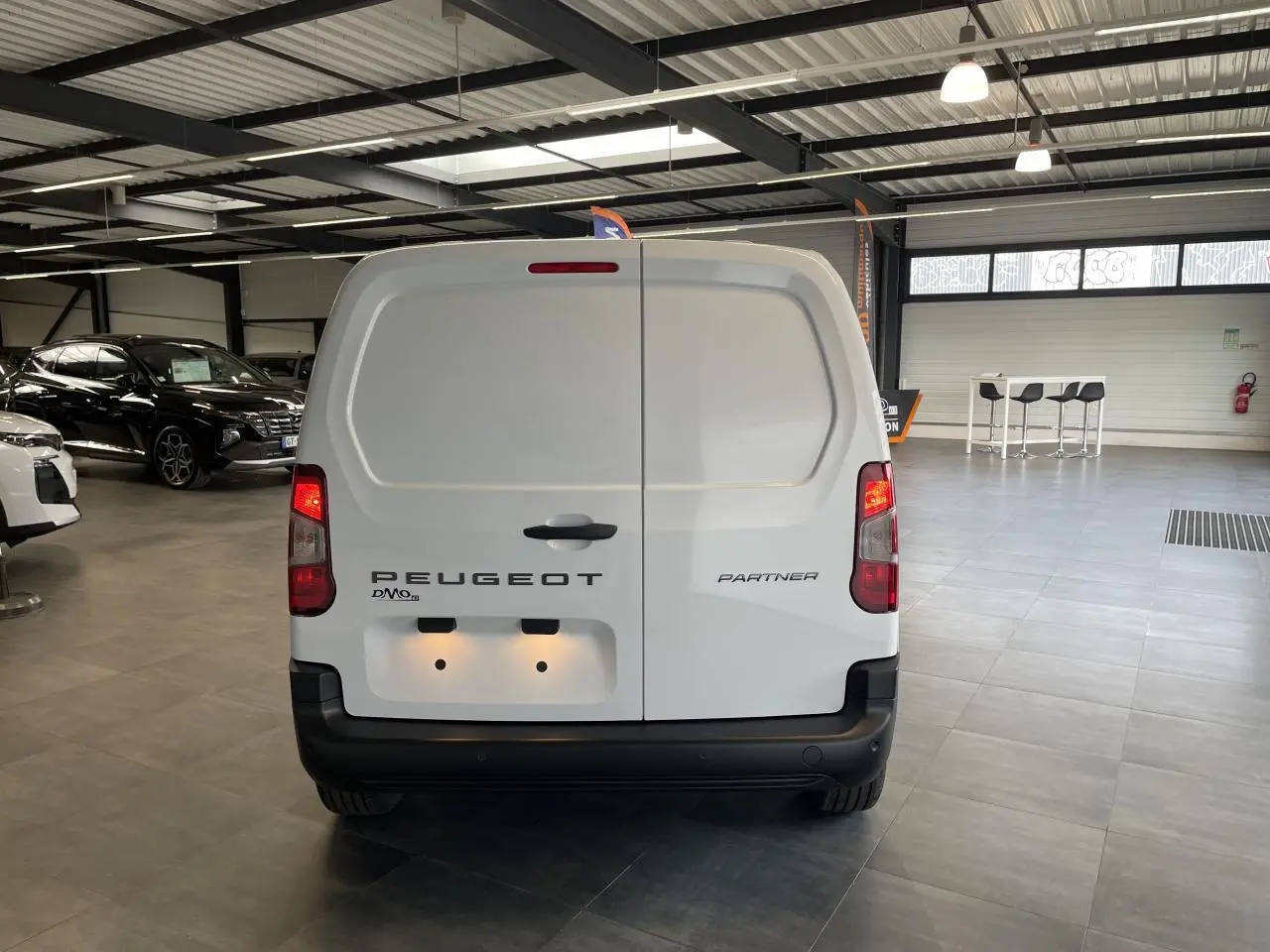 Vue arrière d'un Peugeot Partner blanc stationné en intérieur, avec portes battantes fermées et feux allumés.