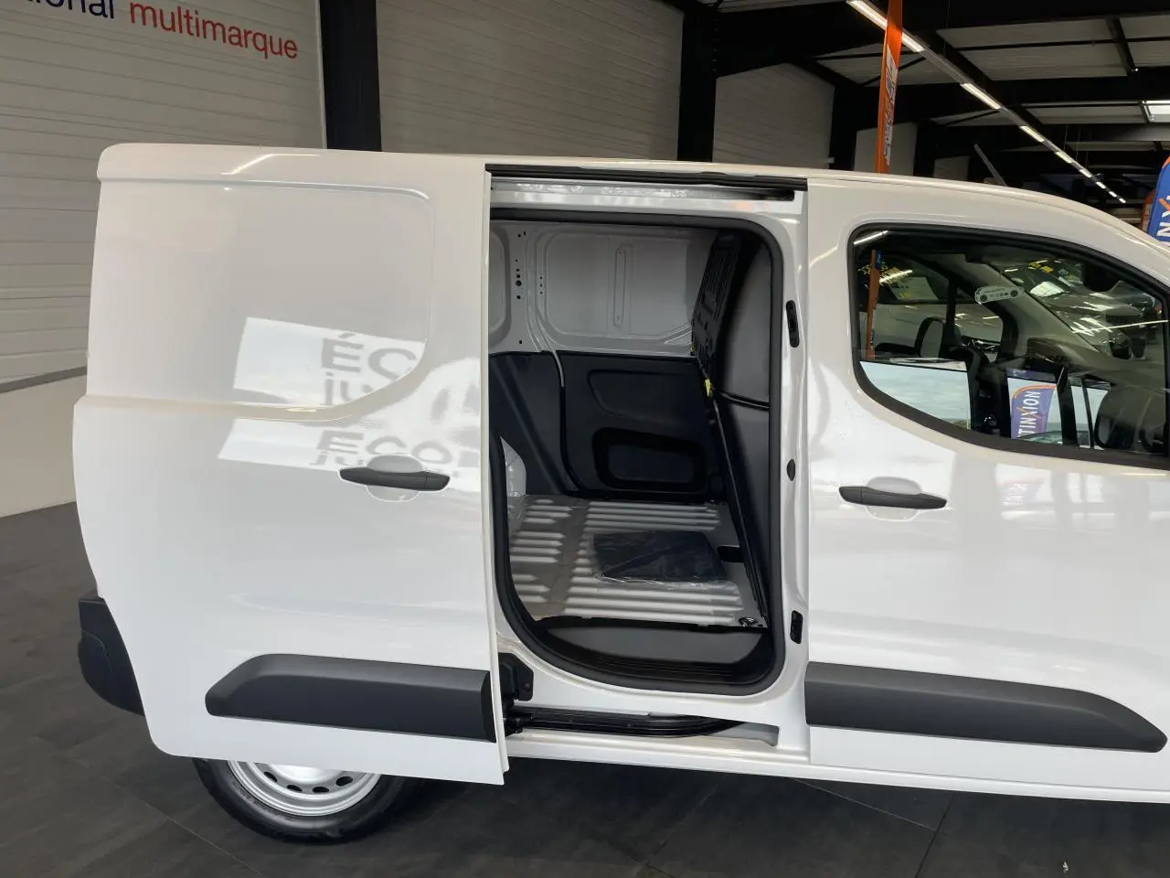 Vue latérale droite d’un Peugeot Partner blanc avec porte coulissante ouverte montrant l’espace de chargement vide.