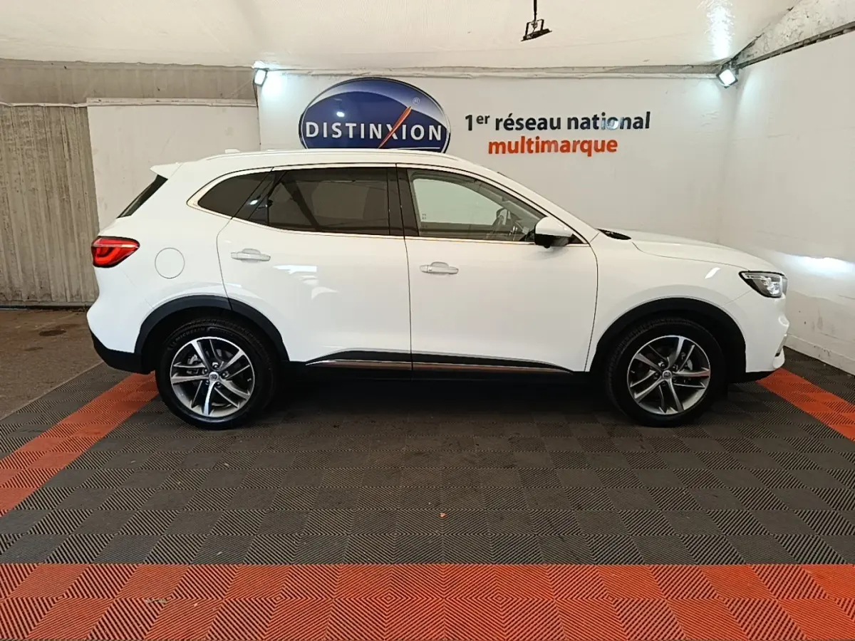Vue de profil côté droit du SUV blanc MG Motor EHS 2023 dans un showroom avec jantes alliage et vitres teintées.