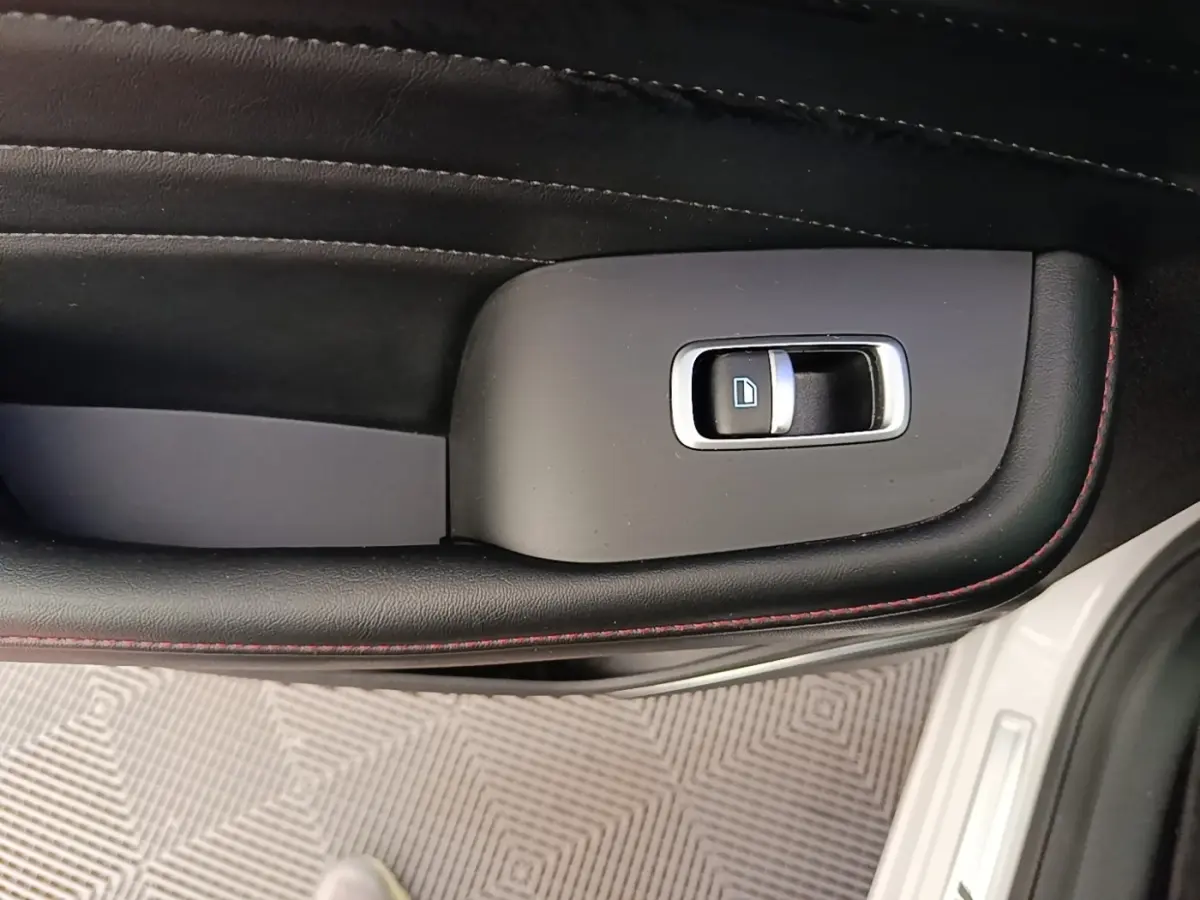 Détail de la commande de lève-vitre côté conducteur sur porte intérieure noire avec surpiqûres rouges d’un MG Motor EHS blanc.