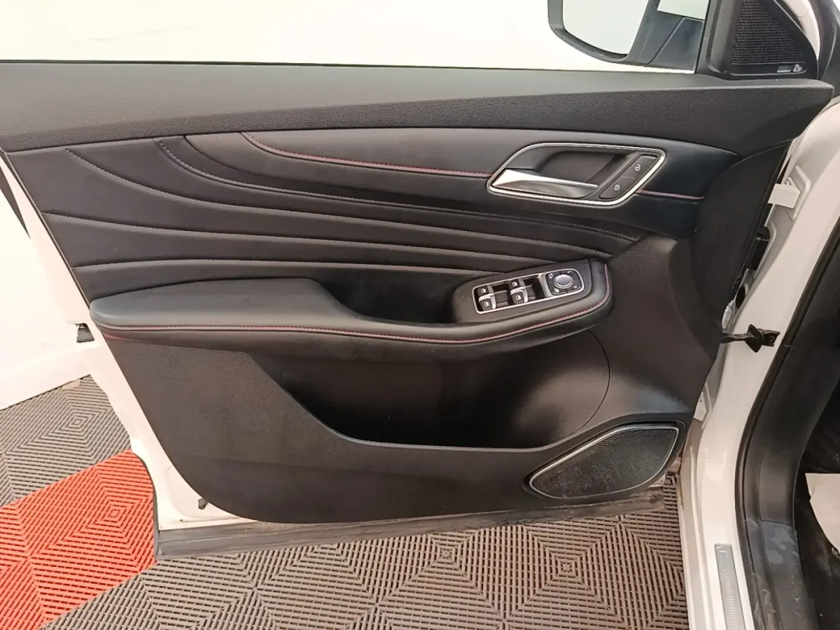 Porte avant gauche ouverte d’un MG Motor EHS blanc, intérieur noir avec surpiqûres rouges et commandes électriques.
