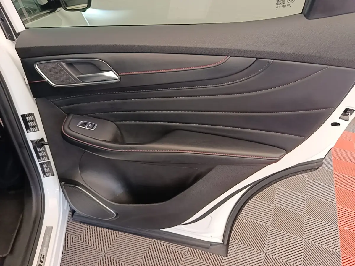 Intérieur de la porte arrière gauche du MG Motor EHS blanc, avec garniture noire et surpiqûres rouges visibles.